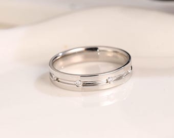 May include: A silver ring with three small, clear gemstones set in a horizontal line. The ring has a simple, elegant design with a polished finish. The band features two parallel grooves, adding a subtle detail to the jewelry.