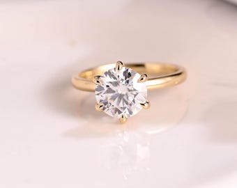 May include: A gold engagement ring with a large, round, clear diamond set in a six-prong setting.