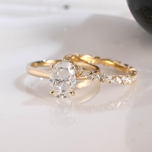 Peut inclure: Une parure de bagues en or composée d'une bague de fiançailles avec une pierre centrale ovale sertie de quatre griffes sur un anneau lisse, accompagnée d'une alliance ornée de petites pierres claires taille marquise et ronde.