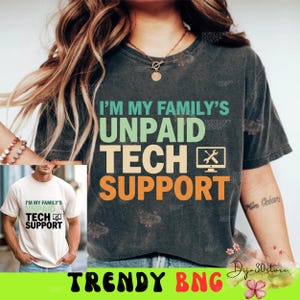 Puede incluir: Camiseta gris oscuro con el texto "I'M MY FAMILY'S UNPAID TECH SUPPORT" en verde, naranja y blanco. El diseño incluye un icono de monitor de ordenador con una llave inglesa y un destornillador. Una imagen más pequeña muestra una camiseta similar.