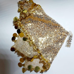 May include: A gold sequined accessory with a sheer fabric base. The edges are trimmed with a gold chain and adorned with dangling gold and brown circular embellishments. Likely used for dance or costume purposes.
