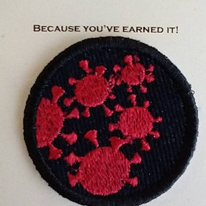 May include: A circular embroidered patch featuring a black background with red virus-like shapes. The patch is mounted on a card with the text MERIT BADGE and BECAUSE YOU'VE EARNED IT! printed in black ink above the circular embroidered design.