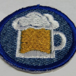 May include: A blue denim patch with a white outline of a beer mug with a white foam top and a gold-colored beer inside.