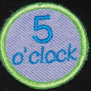 May include: A round, green-trimmed patch with a light blue background. The patch features a blue number "5" and the text "o'clock" in blue.