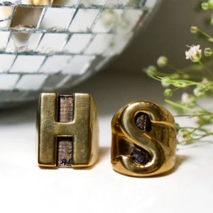 May include: Two gold rings featuring the letters H and S. The rings are chunky and have a textured finish.