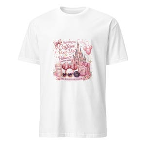 Pode incluir: Uma t-shirt branca com uma impressão gráfica rosa de um castelo, orelhas de rato, uma chávena de café e uma mochila. O texto diz: Running on Caffeine, Pixie Dust & Patience (in that order), Tired Mum, Happy Heart, Magic On e outras frases.