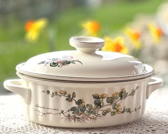 Peut inclure: Plat à gratin ovale en céramique blanche avec un couvercle et deux poignées. Le plat est décoré d'un motif floral avec des feuilles vertes et des fleurs jaunes. Le texte "Lysimachia nummularia" est imprimé sur le plat.