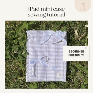 May include: A light blue and white gingham iPad mini case with a white satin ribbon tied in a bow. The case is lying on a bed of green grass. The text "BEGINNER FRIENDLY!" is written on a white paper note.