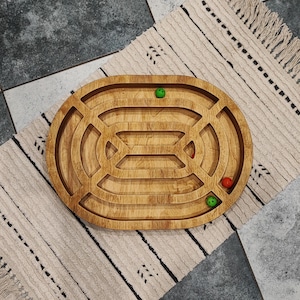 Könnte beinhalten: Ovales Holzlabyrinth mit einer gerillten Bahn zum Rollen von Kugeln. Das Labyrinth hat drei grüne Kugeln und eine rote Kugel.
