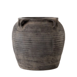 May include: A large, dark brown, unglazed ceramic pot with two handles on the rim. The pot has a textured, slightly rough surface.