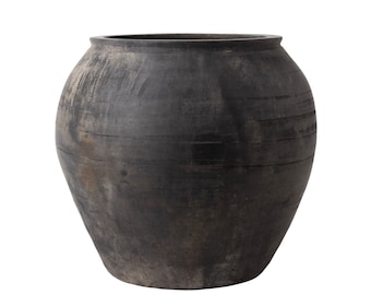 May include: A large, round, black clay pot with a wide opening. The pot has a rustic, aged appearance with visible lines and texture.