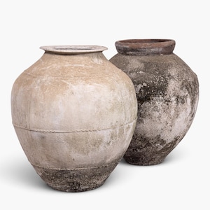 Peut inclure: Deux grands récipients en terre cuite, ronds et à large ouverture, avec une surface texturée et patinée. Le récipient au premier plan est beige clair avec une base sombre et tachetée, tandis que celui derrière est gris foncé et brun.