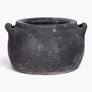 May include: A matte black, wide-mouthed ceramic pot with a rounded body and two integrated side handles. The surface features a textured, weathered finish with subtle variations in tone and small, light-colored flecks across the exterior.