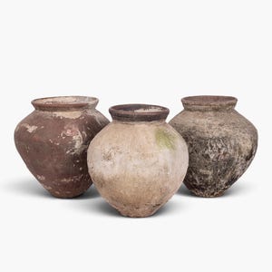 May include: Three round earthenware pots with wide openings and tapered bases. The left pot is reddish-brown, the center pot is light beige with a green patch, and the right pot is dark grey and textured with a weathered, aged appearance.