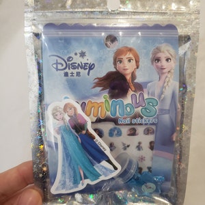 May include: A clear plastic bag with a holographic finish containing a set of Frozen nail stickers. The bag features a colorful image of Elsa and Anna from the Disney movie Frozen. The text "Disney" and "Nail Stickers" are visible on the packaging.