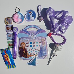 May include: A Frozen II themed gift bag filled with various items, including a purple hair tie, a purple beaded bracelet, a lollipop, a sticker sheet, a small plastic container with a lid, a small plastic toy, a candy bar, and a small plastic toy. The bag is decorated with a picture of Elsa and Anna from Frozen II.