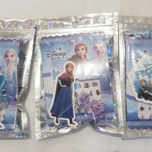 May include: Three plastic bags with different Disney Frozen themed sticker sets. Each bag features a different character from the movie, including Anna, Elsa, and Olaf. The bags are decorated with glitter and have a blue and white color scheme.