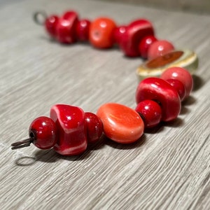 May include: A red, orange, and green ceramic bead bracelet with a metal clasp. The beads are various shapes and sizes.