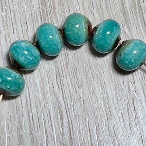May include: A strand of turquoise blue ceramic beads with white flecks, strung on a copper wire.