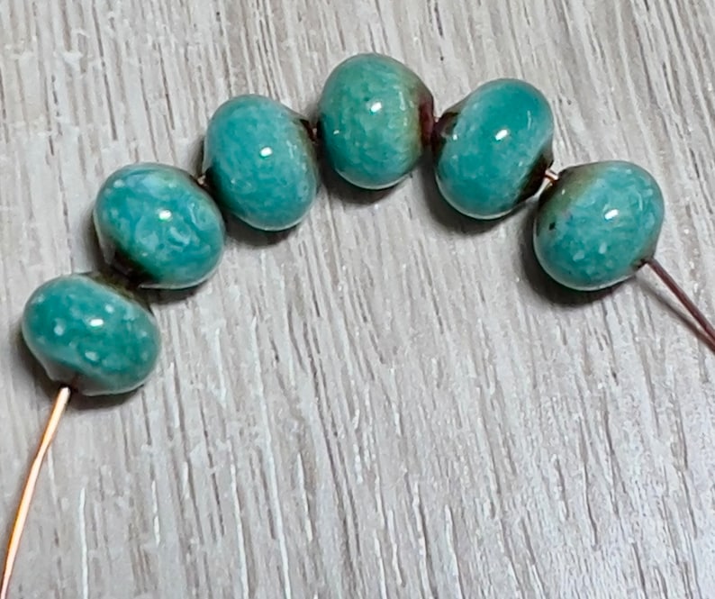 May include: A strand of turquoise blue ceramic beads with white flecks, strung on a copper wire.