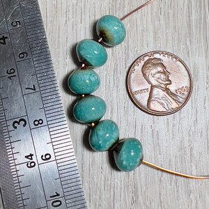 May include: A strand of turquoise blue ceramic beads with a mottled finish. The beads are strung on a thin wire and are approximately the size of a US penny.
