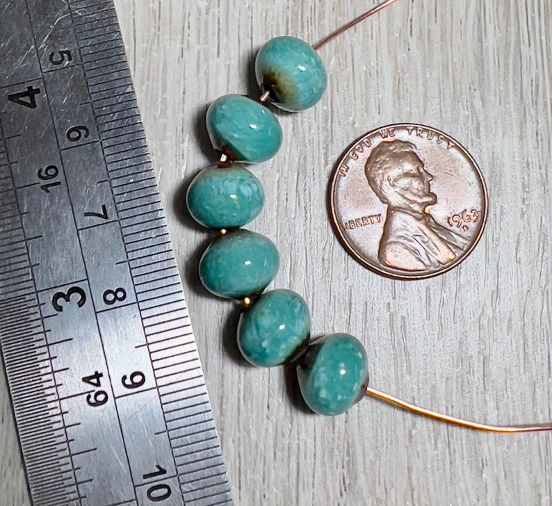 May include: A strand of turquoise blue ceramic beads with a mottled finish. The beads are strung on a thin wire and are approximately the size of a US penny.