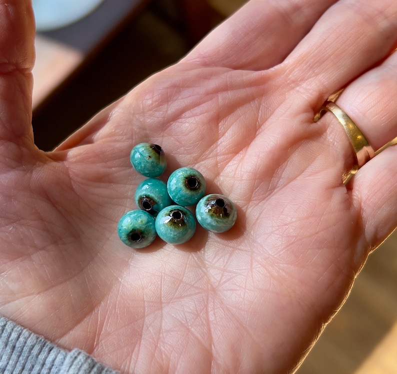 May include: A collection of six turquoise ceramic beads with black centers. The beads are round and have a glossy finish.