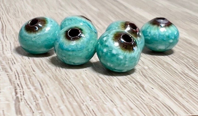 May include: A group of six turquoise and brown ceramic beads with a hole in the center. The beads have a speckled and glazed finish.