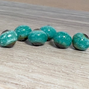 May include: Six green and brown ceramic beads with a mottled, marbled effect. The beads are round and have a smooth, glossy finish.