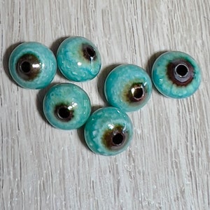 May include: Six turquoise blue ceramic beads with a brown center hole. The beads have a mottled, textured surface.