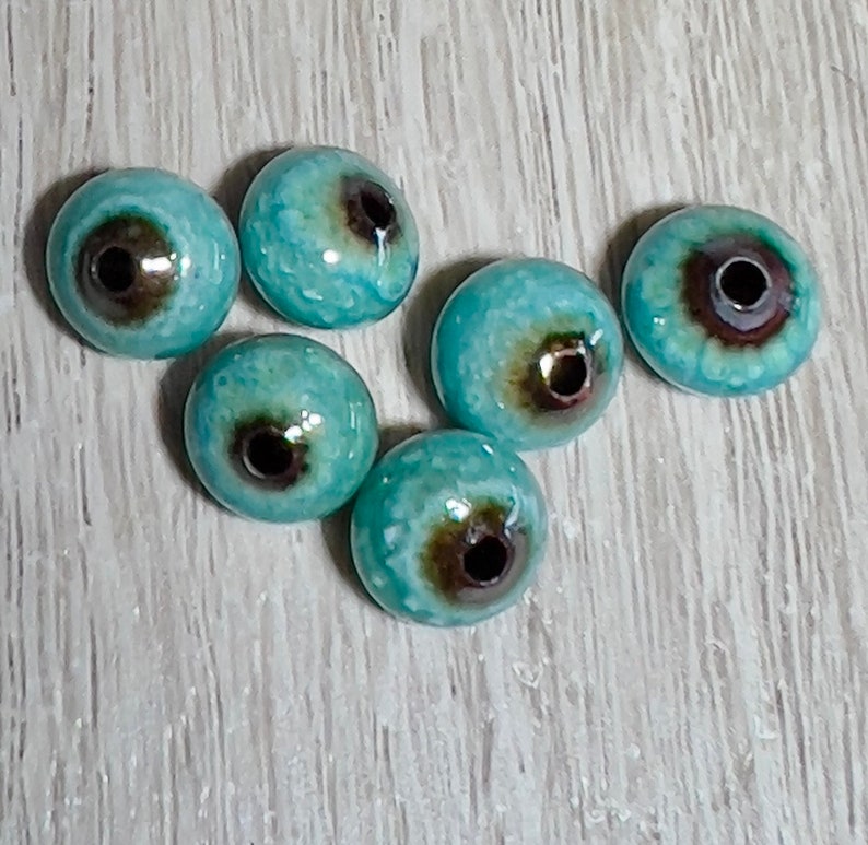 May include: Six turquoise blue ceramic beads with a brown center hole. The beads have a mottled, textured surface.