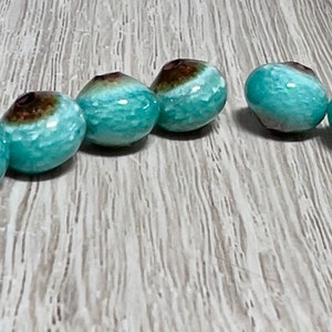 May include: Six teal blue and brown ceramic beads with a glossy finish. The beads are round and have a hole in the center for stringing.