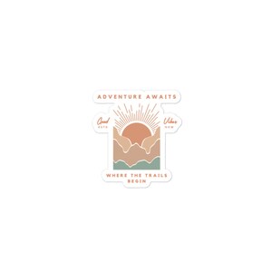 May include: A sticker featuring a sunset over mountains with the text "Adventure Awaits" at the top, "Good Vibes Now" on the sides, and "Where the Trails Begin" at the bottom.