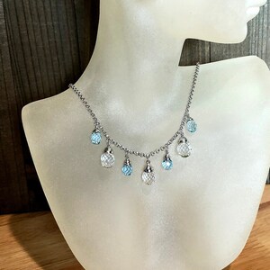May include: A silver chain necklace with dangling crystal beads. The beads are clear and light blue.