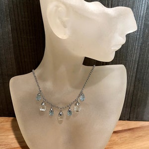 May include: A silver chain necklace with teardrop-shaped blue and clear crystal pendants.