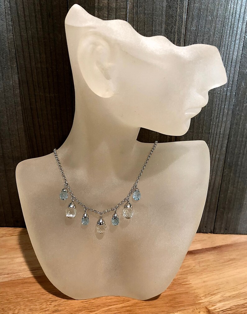 May include: A silver chain necklace with teardrop-shaped blue and clear crystal pendants.