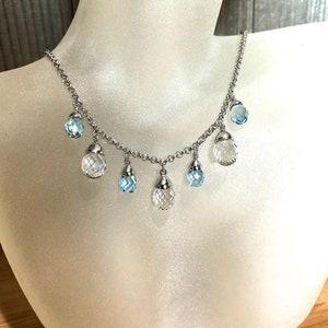 May include: A silver chain necklace with clear and light blue faceted gemstone drops. The necklace is displayed on a white mannequin bust.