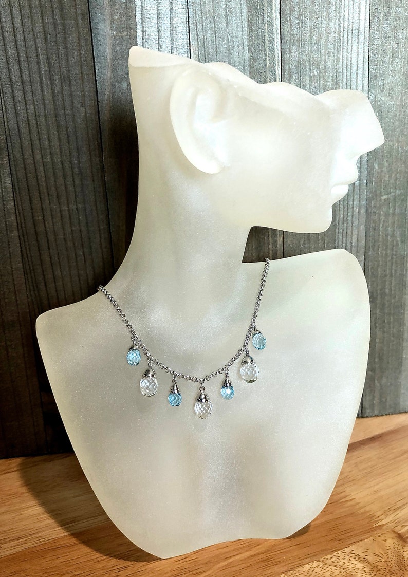 May include: A silver chain necklace with dangling crystal beads. The beads are clear and light blue.