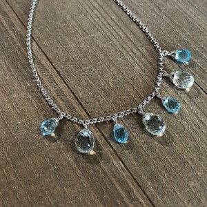 May include: A silver chain necklace with multiple teardrop-shaped blue topaz gemstones hanging from it.