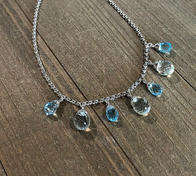 May include: A silver chain necklace with multiple teardrop-shaped blue topaz gemstones hanging from it.