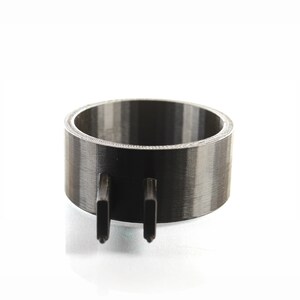 K&ouml;nnte beinhalten: Ein schwarzer und grauer 3D-gedruckter Ring mit zwei Zacken, die von unten herausragen.
