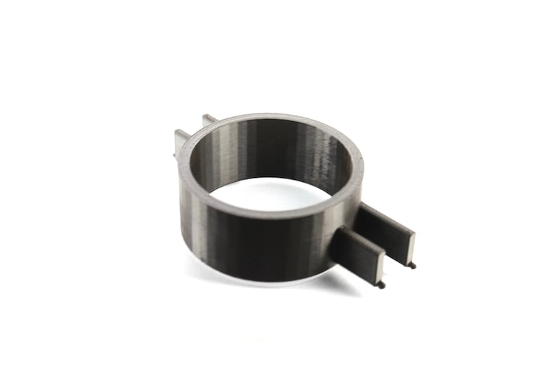 K&ouml;nnte beinhalten: Ein schwarzer und grauer 3D-gedruckter Ring mit einer strukturierten Oberfl&auml;che. Der Ring hat ein kleines, flaches, rechteckiges St&uuml;ck, das seitlich herausragt.