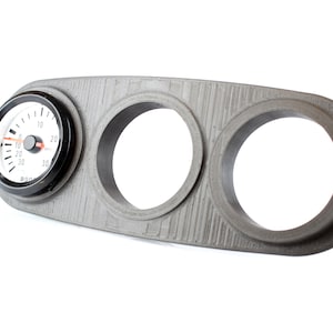 May include: A gray plastic panel with three circular cutouts for gauges. One cutout has a black and white gauge with a red needle and the text "BOOST" printed on the face.
