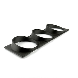 May include: A black, 3-hole gauge pod, likely for a car's dashboard. The pod is made of a matte black material and has three circular openings. The base is rectangular, and the openings are angled towards the viewer.