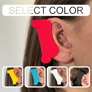May include: A red ear support device is shown in use, with a selection of other colors displayed below. The text "SELECT COLOR" is at the top. The device appears to be made of a flexible material and is designed to support the ear.