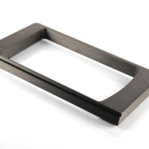 Puede incluir: Un marco de plástico negro para un teléfono u otro dispositivo electrónico. El marco está hecho de un material texturizado y tiene una forma rectangular.