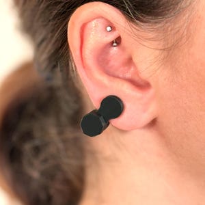 Puede incluir: Túneles para la oreja negros de forma geométrica. Los túneles tienen una parte delantera hexagonal y una parte trasera redondeada, conectadas por una pieza cilíndrica corta. Los túneles se usan en una oreja perforada.