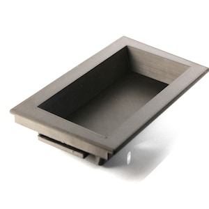 May include: A gray plastic drawer pull with a rectangular opening. The pull has a smooth, slightly textured surface.