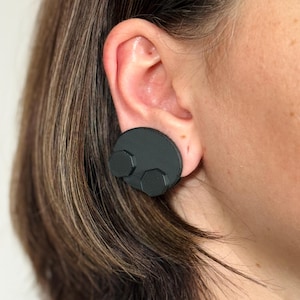 May include: A pair of black earrings with a round, textured base and three hexagonal shapes attached.