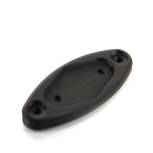 Puede incluir: Un componente negro de forma ovalada con dos agujeros circulares en los extremos y un agujero más pequeño en el centro. El componente tiene una superficie ligeramente texturizada y parece estar hecho de plástico. El objeto está aislado sobre un fondo blanco.